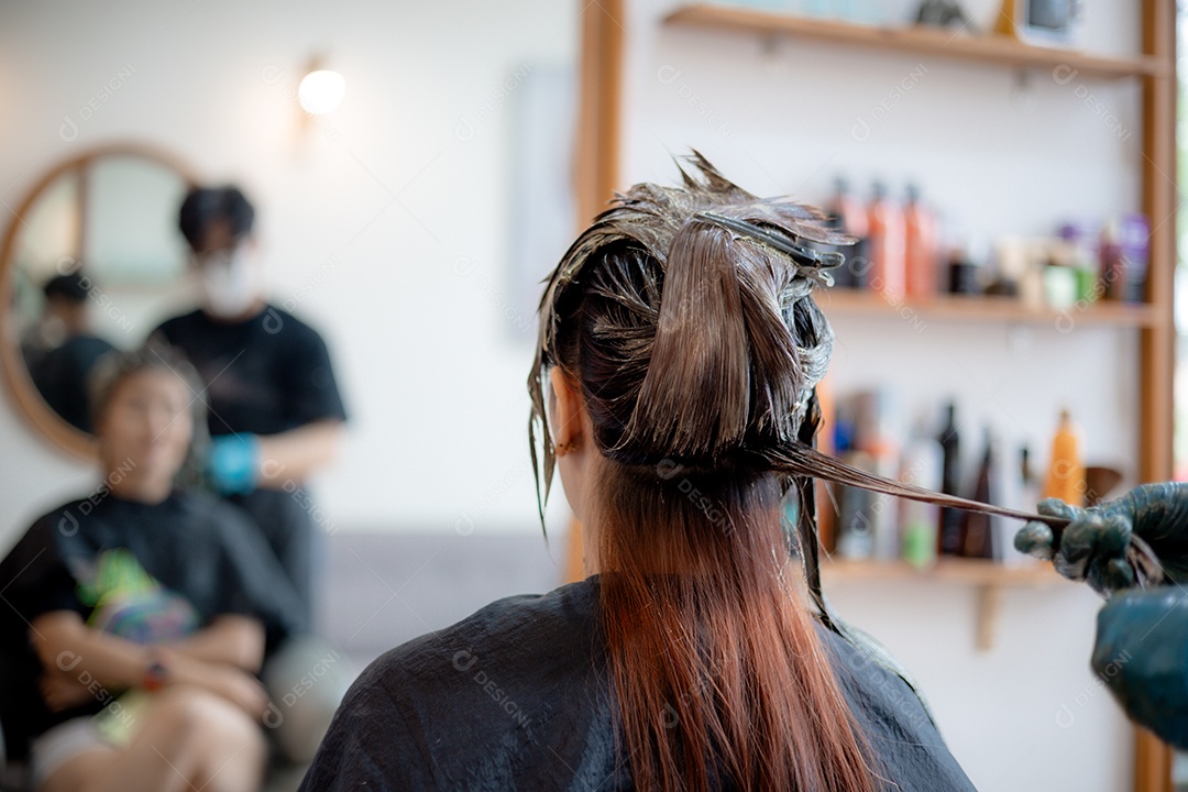 O cabelereiro está usando luvas e um pincel para aplicar tintura nos cabelos da mulher