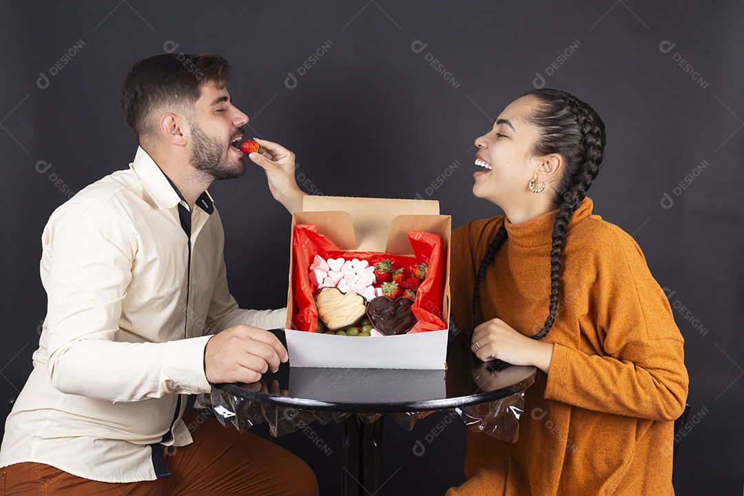 Casal se divertindo comendo doces e frutas de caixa de presente de dia dos namorados