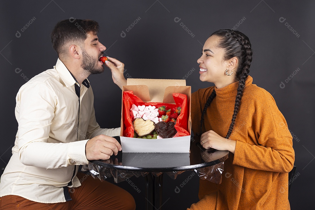 Casal se divertindo comendo doces e frutas de caixa de presente de dia dos namorados