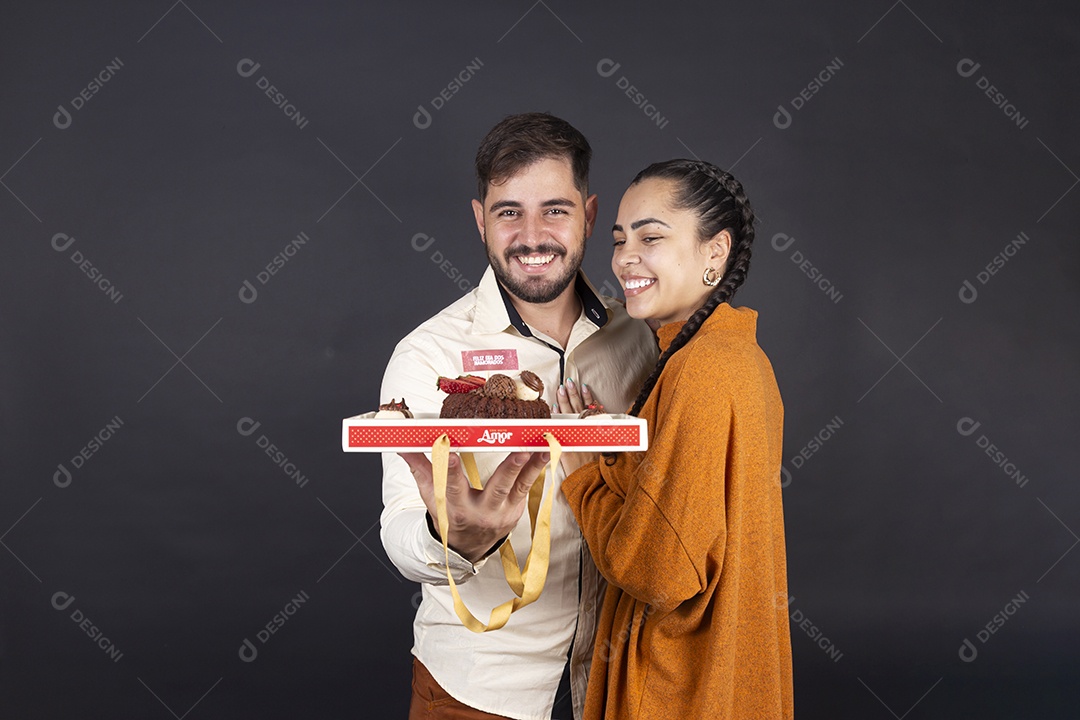 Casal segurando caixa de doces e sorrindo comemorando dia dos namorados