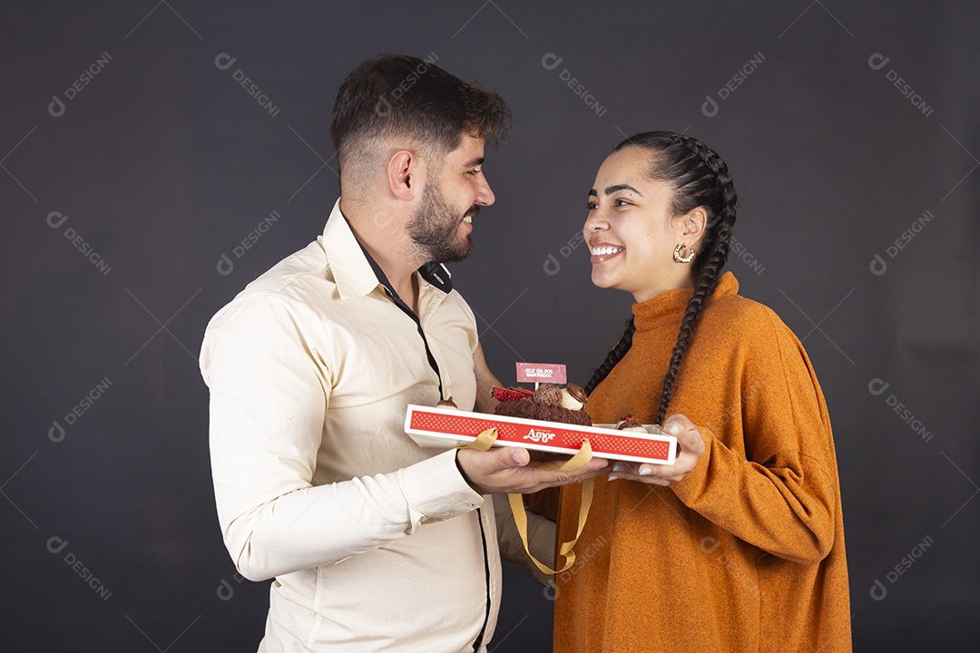 Casal feliz se olhando e segurando caixa de doces sobre fundo escuro