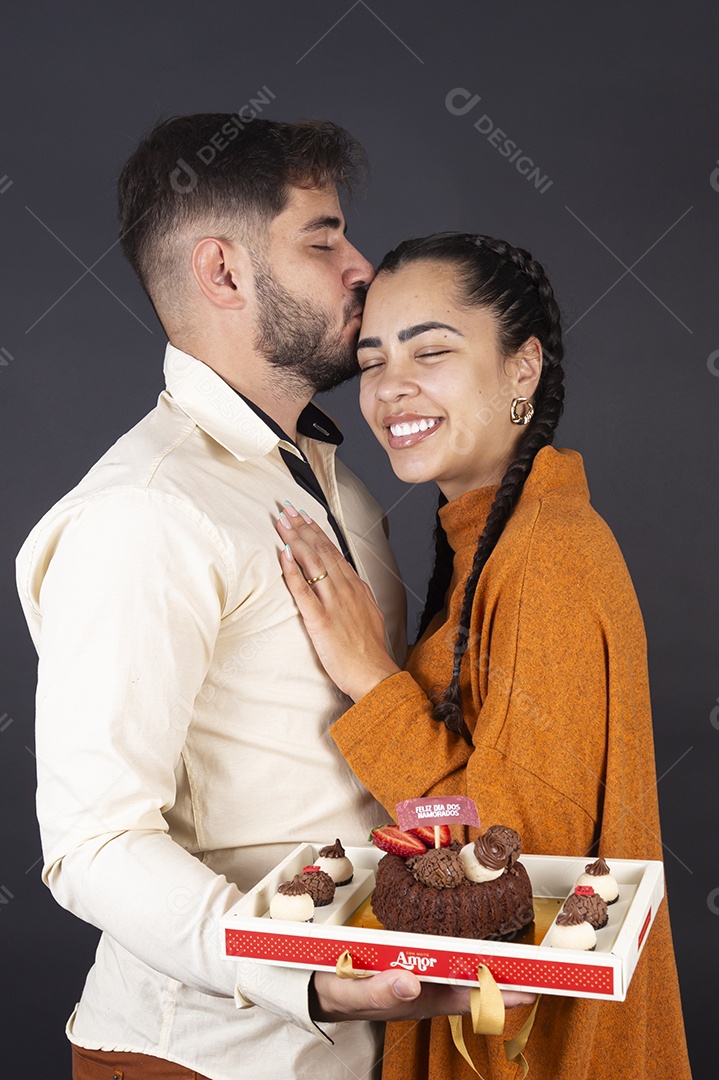 Homem beijando sua namorada segurando bolo para comemorar dia dos namorados