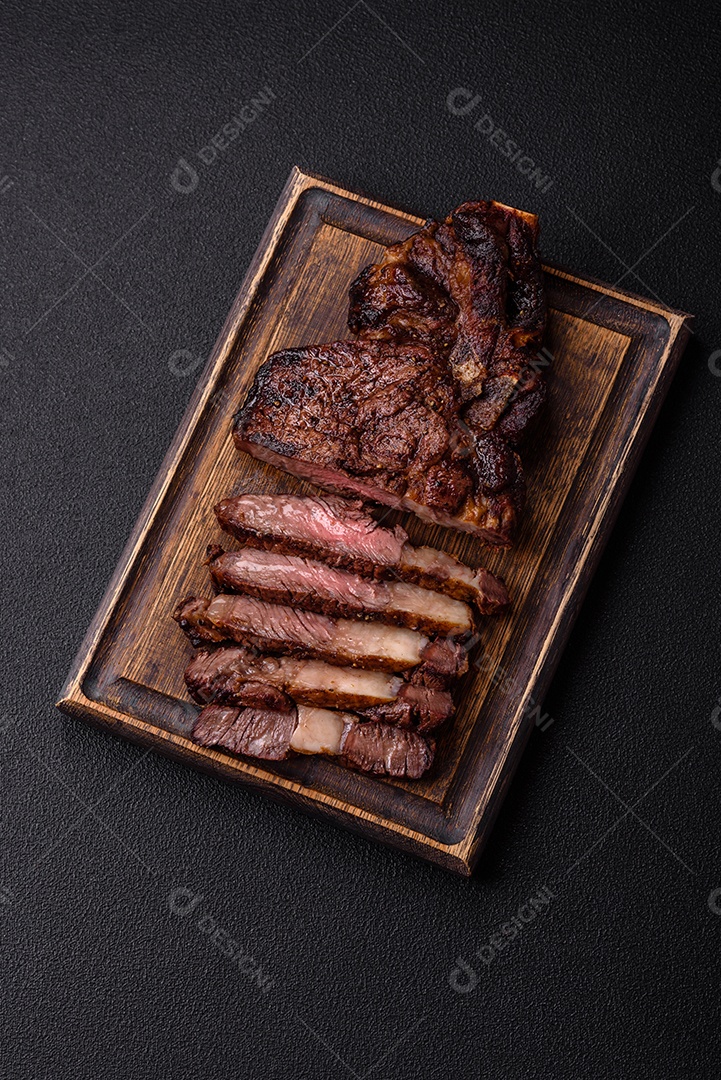 Delicioso bife suculento de lombo grelhado com sal, especiarias e ervas em um fundo escuro de concreto