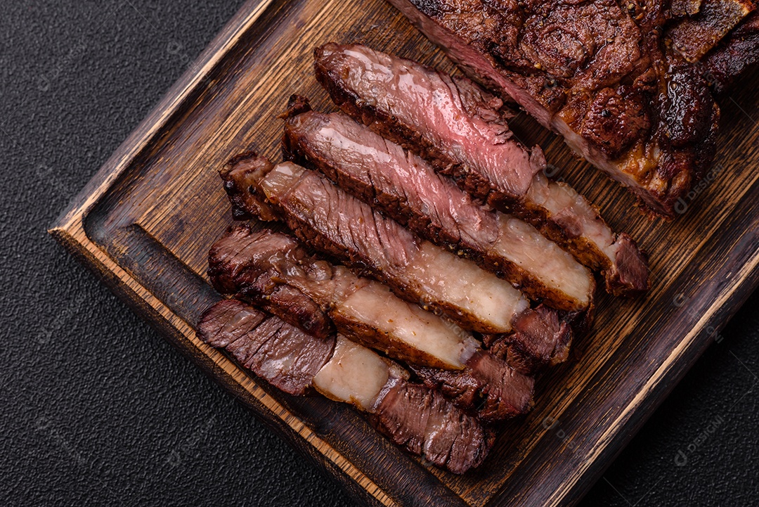 Delicioso bife suculento de lombo grelhado com sal, especiarias e ervas em um fundo escuro de concreto