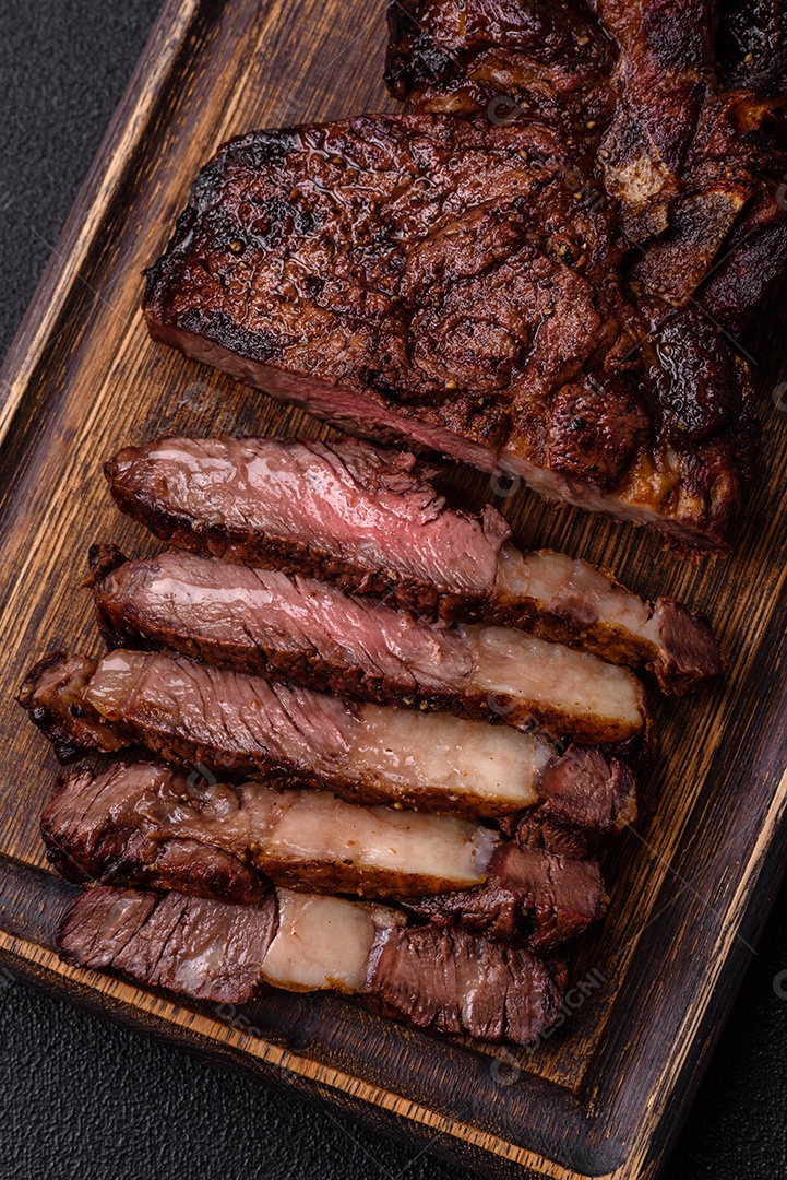 Delicioso bife suculento de lombo grelhado com sal, especiarias e ervas em um fundo escuro de concreto