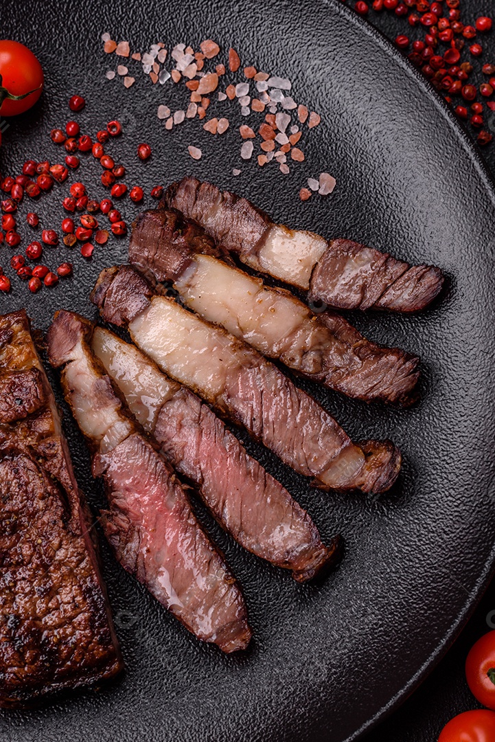 Delicioso bife suculento de lombo grelhado com sal, especiarias e ervas em um fundo escuro de concreto