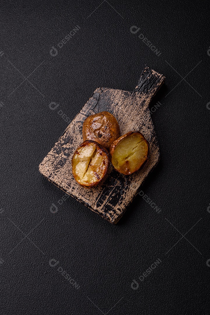 Deliciosas batatas cortadas ao meio grelhadas com sal, especiarias e ervas sobre um fundo escuro de concreto