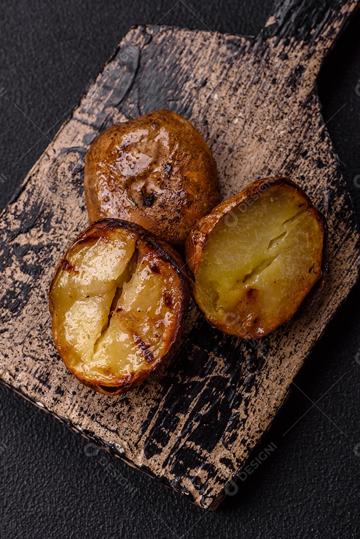 Deliciosas batatas cortadas ao meio grelhadas com sal, especiarias e ervas sobre um fundo escuro de concreto