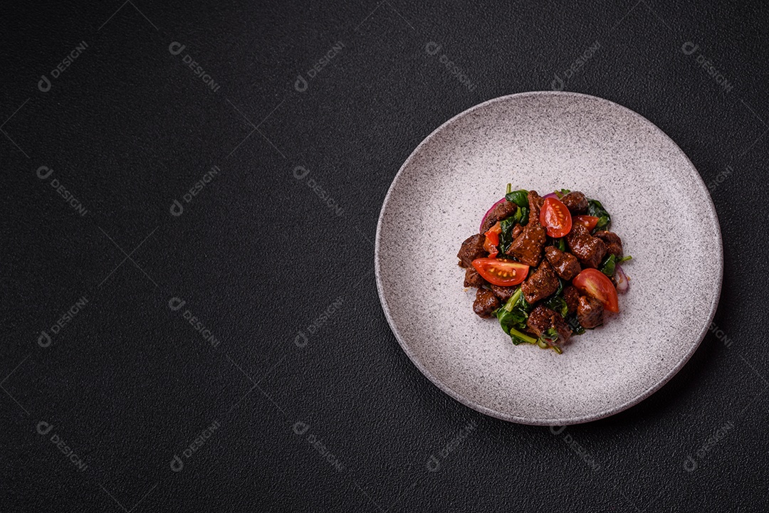 Deliciosa salada quente com pedaços de carne, espinafre, tomate, sal, especiarias e ervas sobre um fundo escuro de concreto