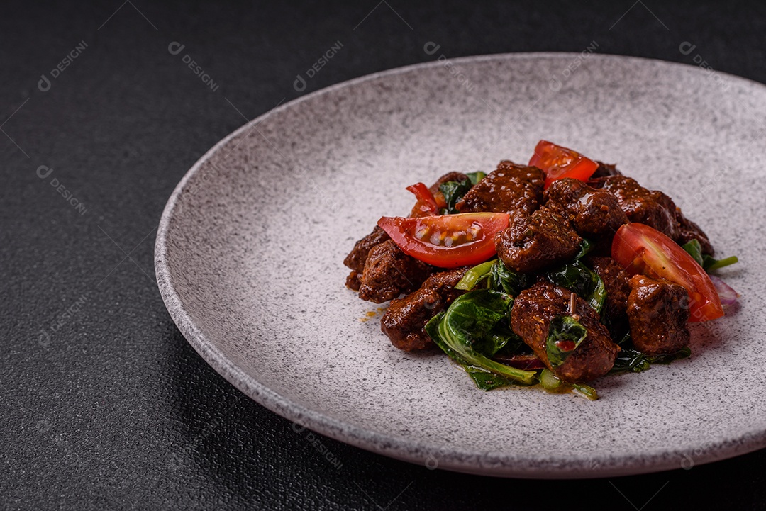 Deliciosa salada quente com pedaços de carne, espinafre, tomate, sal, especiarias e ervas sobre um fundo escuro de concreto