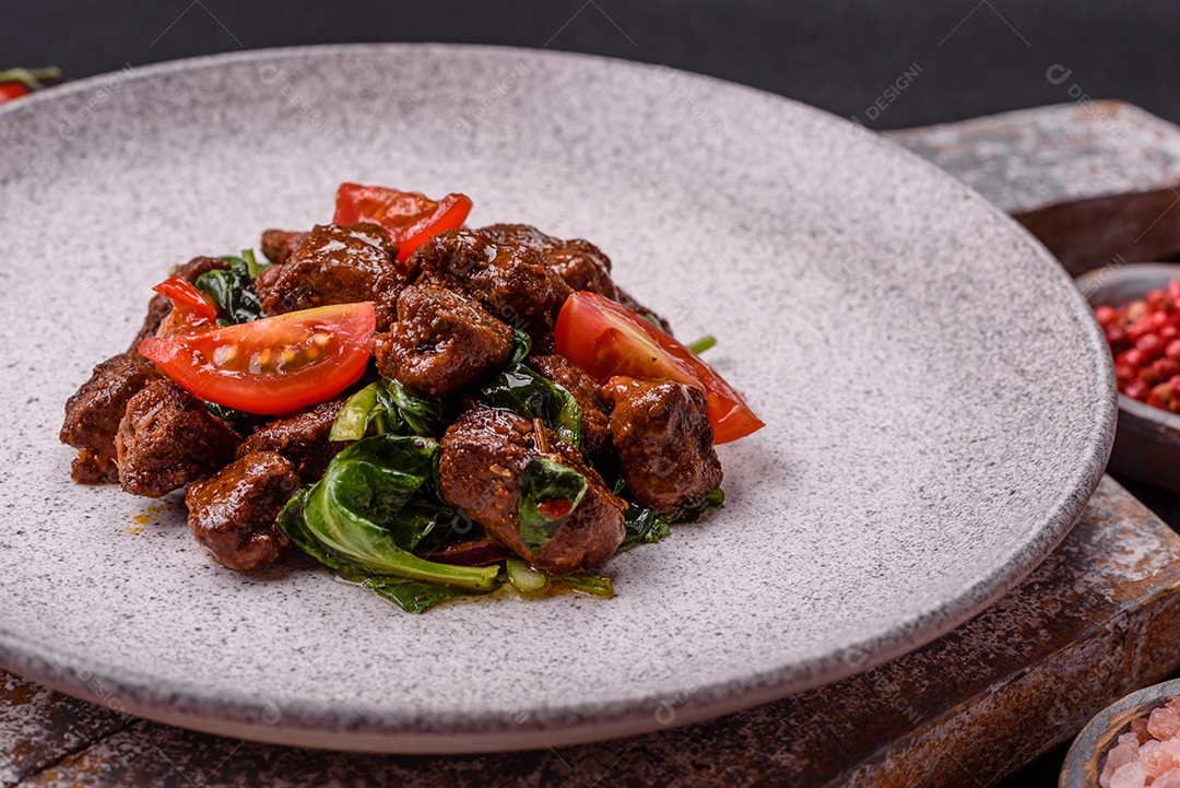 Deliciosa salada quente com pedaços de carne, espinafre, tomate, sal, especiarias e ervas sobre um fundo escuro de concreto