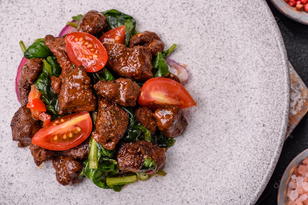 Deliciosa salada quente com pedaços de carne, espinafre, tomate, sal, especiarias e ervas sobre um fundo escuro de concreto