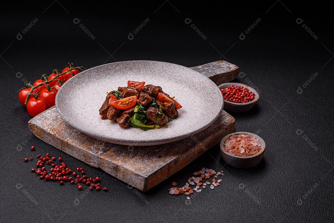 Deliciosa salada quente com pedaços de carne, espinafre, tomate, sal, especiarias e ervas sobre um fundo escuro de concreto