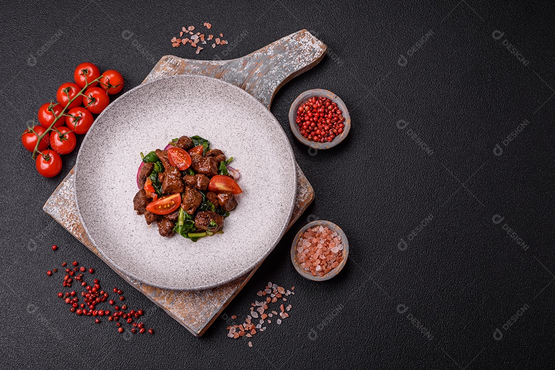 Deliciosa salada quente com pedaços de carne, espinafre, tomate, sal, especiarias e ervas sobre um fundo escuro de concreto