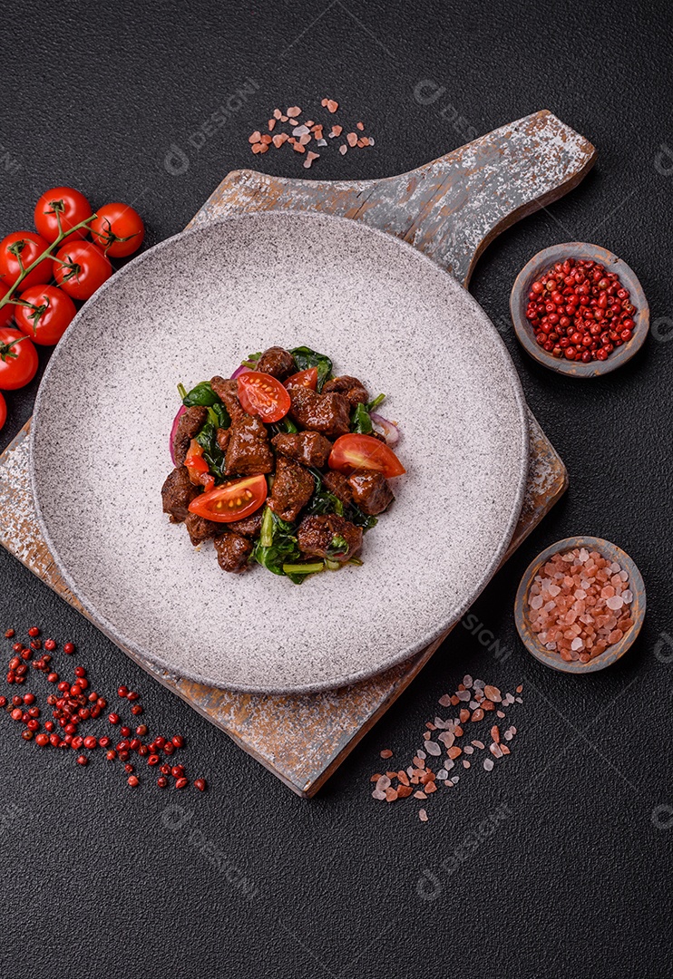 Deliciosa salada quente com pedaços de carne, espinafre, tomate, sal, especiarias e ervas sobre um fundo escuro de concreto