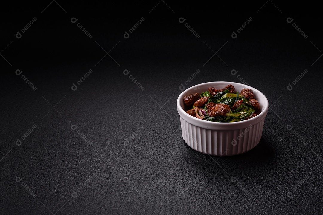 Deliciosa salada quente com pedaços de carne, espinafre, tomate, sal, especiarias e ervas sobre um fundo escuro de concreto