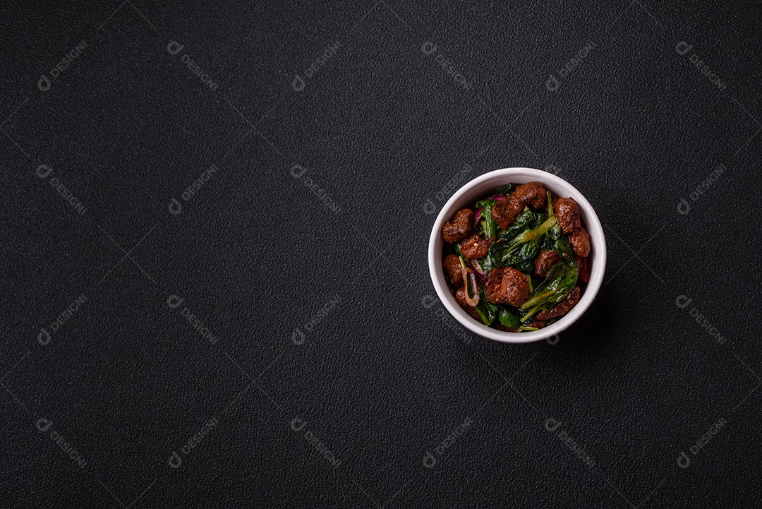Deliciosa salada quente com pedaços de carne, espinafre, tomate, sal, especiarias e ervas sobre um fundo escuro de concreto
