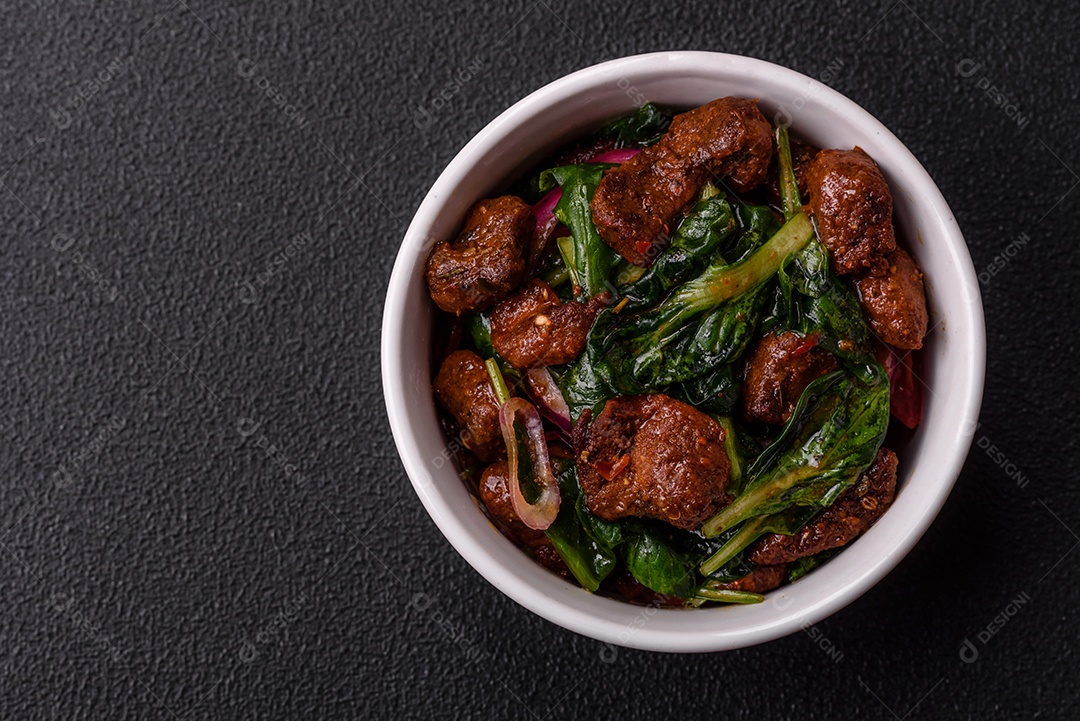 Deliciosa salada quente com pedaços de carne, espinafre, tomate, sal, especiarias e ervas sobre um fundo escuro de concreto