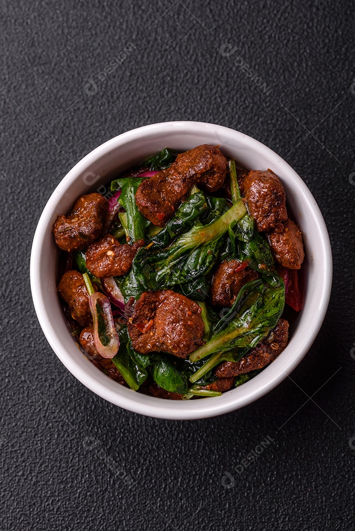 Deliciosa salada quente com pedaços de carne, espinafre, tomate, sal, especiarias e ervas sobre um fundo escuro de concreto