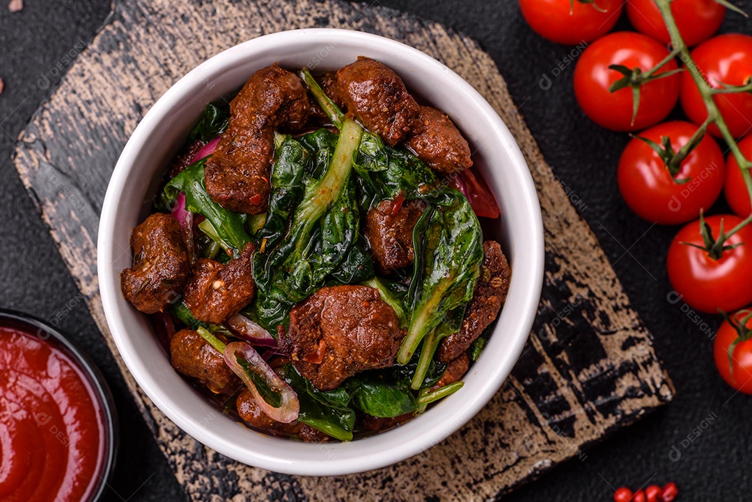 Deliciosa salada quente com pedaços de carne, espinafre, tomate, sal, especiarias e ervas sobre um fundo escuro de concreto