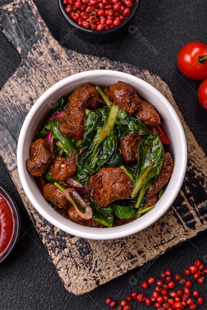 Deliciosa salada quente com pedaços de carne, espinafre, tomate, sal, especiarias e ervas sobre um fundo escuro de concreto