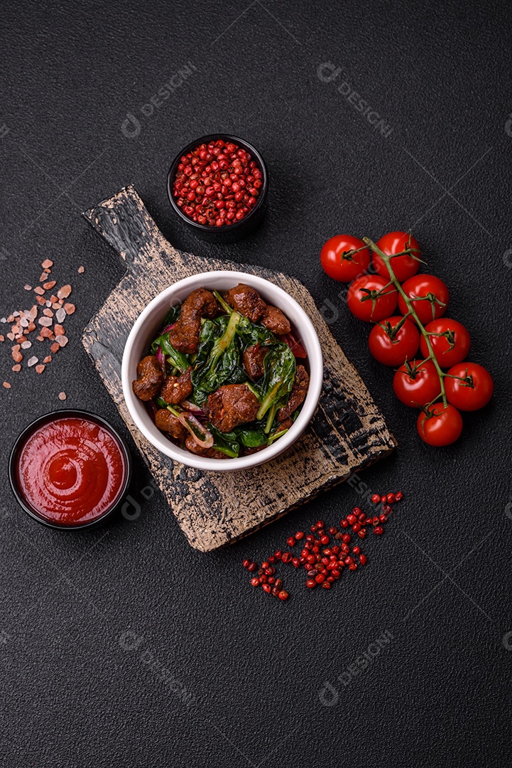Deliciosa salada quente com pedaços de carne, espinafre, tomate, sal, especiarias e ervas sobre um fundo escuro de concreto