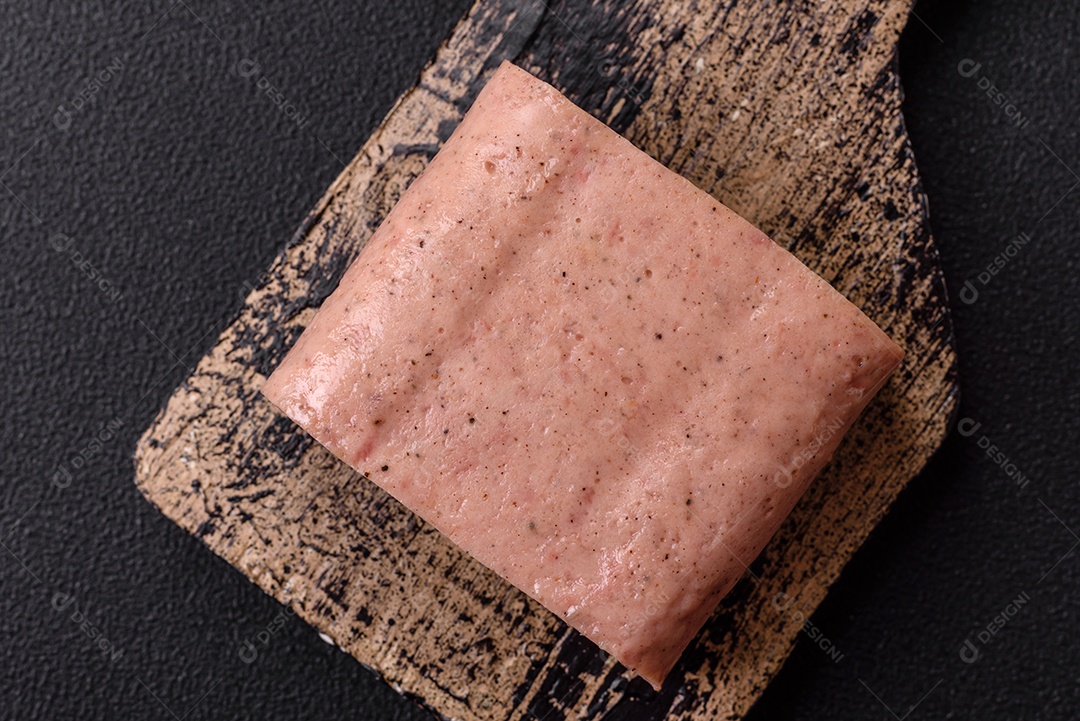 Delicioso presunto rosa enlatado com sal, especiarias e ervas sobre um fundo escuro de concreto