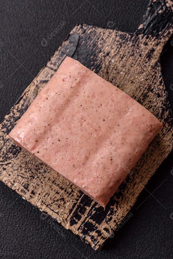 Delicioso presunto rosa enlatado com sal, especiarias e ervas sobre um fundo escuro de concreto