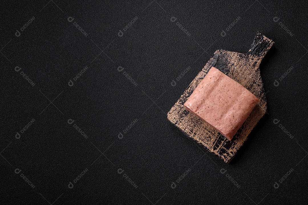 Delicioso presunto rosa enlatado com sal, especiarias e ervas sobre um fundo escuro de concreto