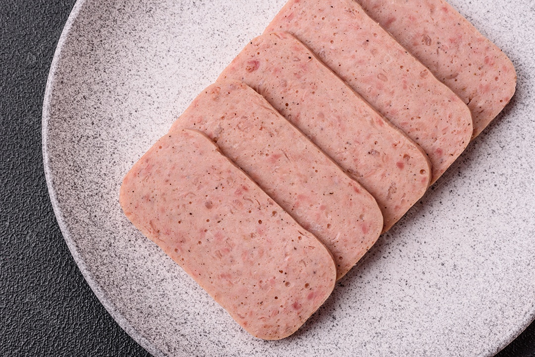Delicioso presunto rosa enlatado com sal, especiarias e ervas sobre um fundo escuro de concreto