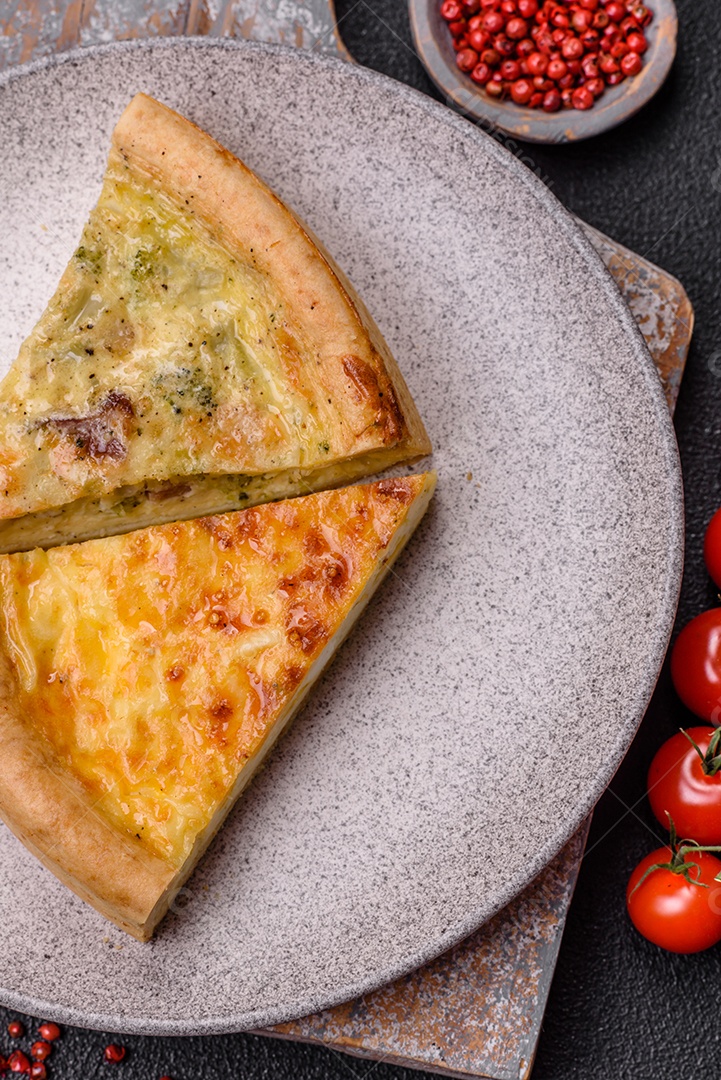 Deliciosa quiche com brócolis, frango ou salmão e queijo com sal e especiarias sobre fundo escuro de concreto