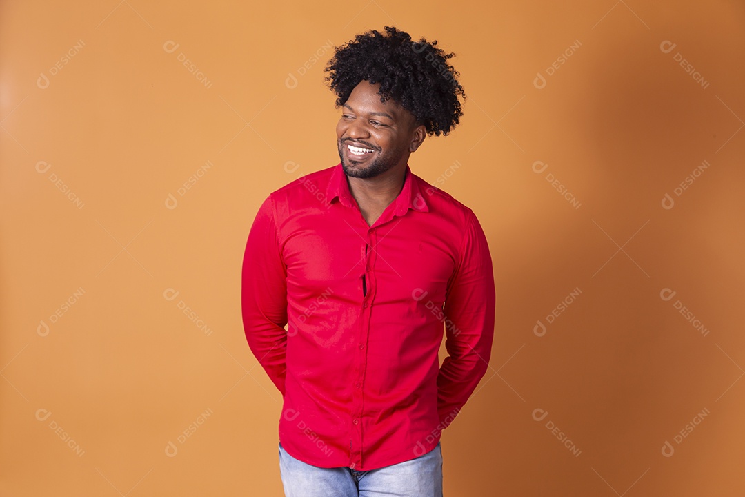 Homem de camiseta vermelha sorrindo com as mãos pra trás