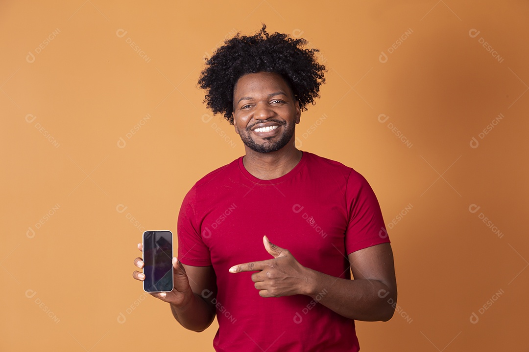 Homem moreno de camiseta vermelha segurando celular e apontando para ele