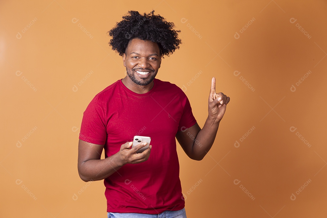 Homem de camiseta vermelha segurando celular e sorrindo apontando para cima