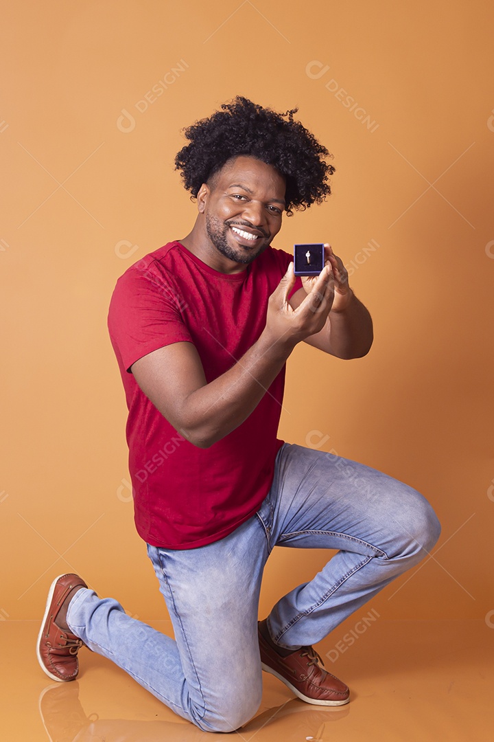 Homem moreno ajoelhado com caixa de aliança