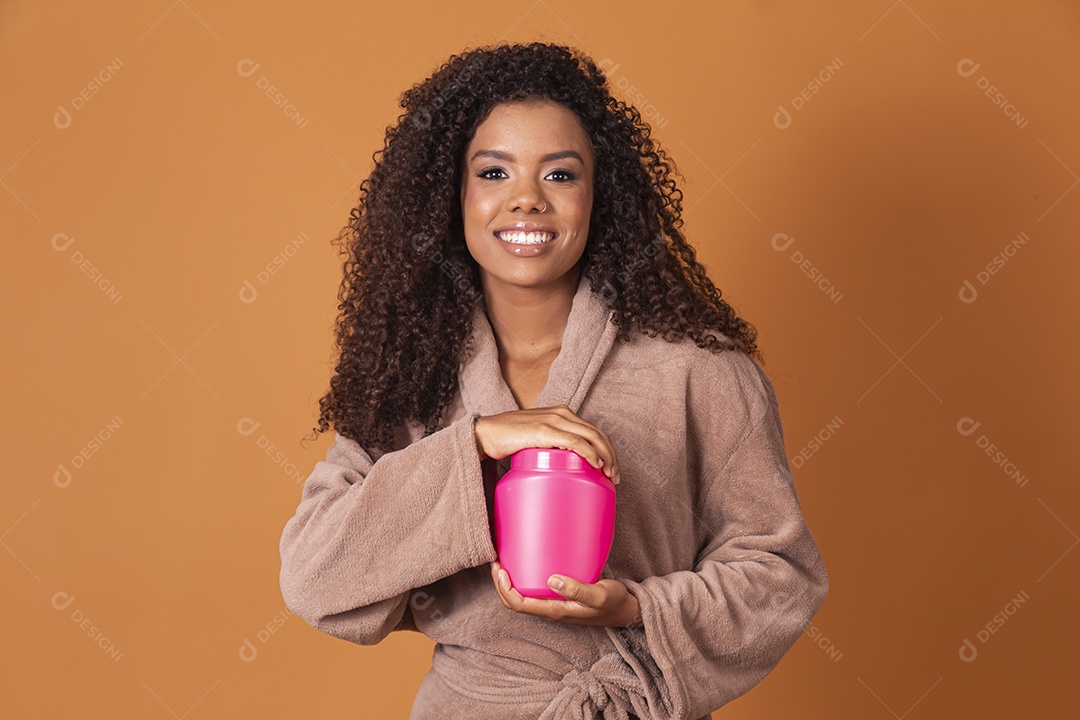 Jovem sorrindo de cabelos cacheado com pote de creme