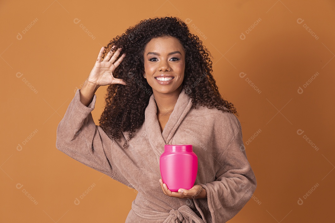 Jovem linda cacheada com pote de creme sobre fundo marrom claro