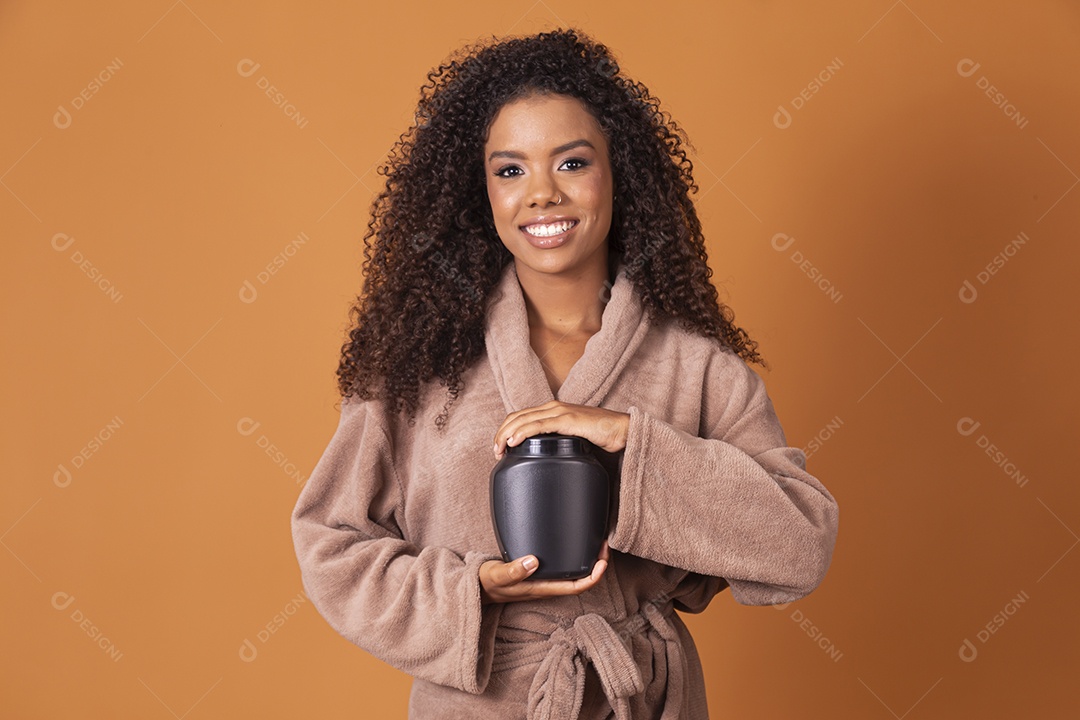 Jovem linda cacheada com pote de creme sobre fundo marrom claro