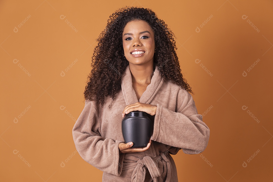 Jovem linda cacheada com pote de creme sobre fundo marrom claro