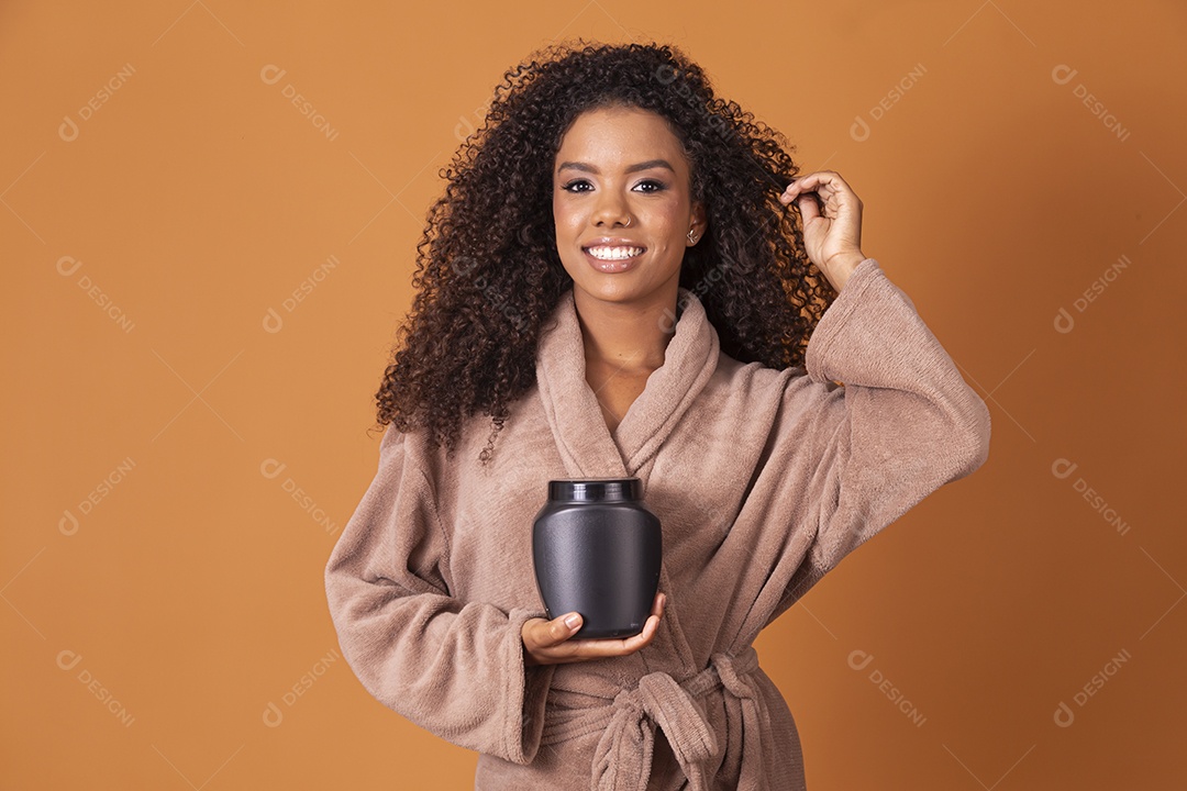 Jovem bonita cacheada com pote de creme sobre fundo marrom claro