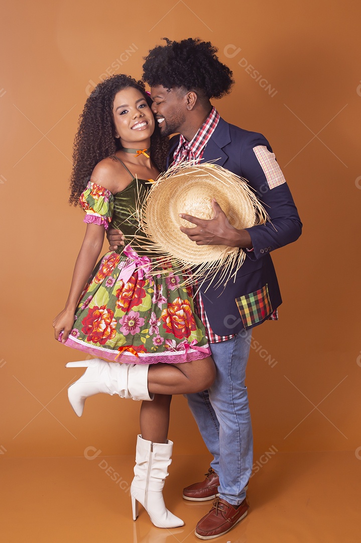 Casal se abraçando sobre fundo alaranjado trajado para quadrilha