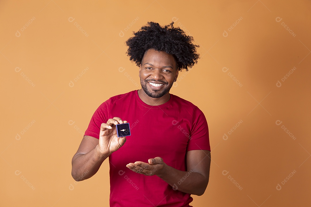 Homem moreno de camiseta vermelha segurando caixa com aliança