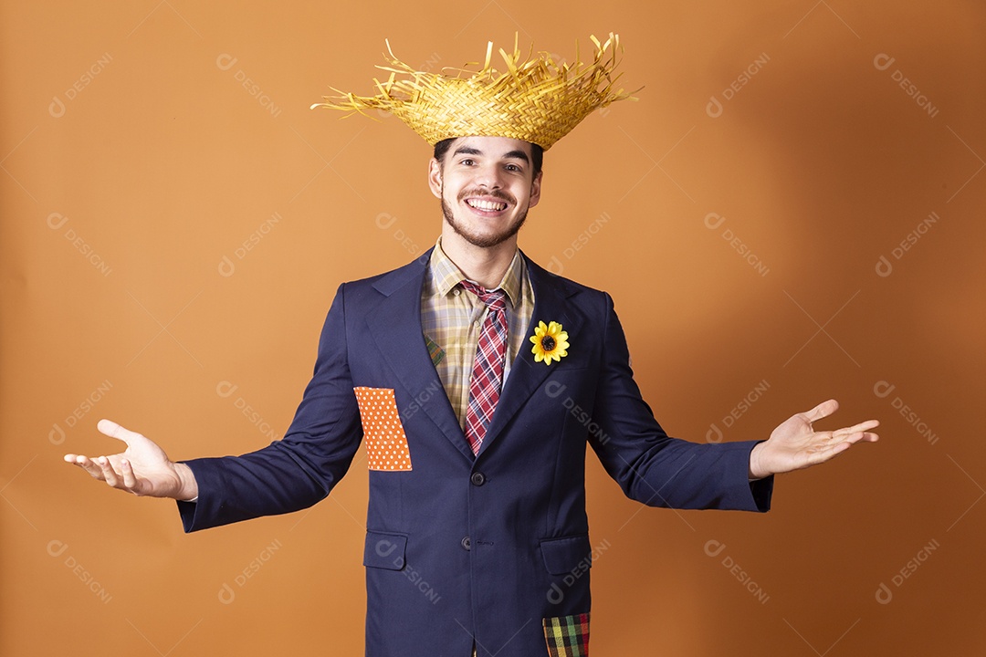 Jovem rapaz sorridente vestido a caráter para festa junina com chapéu nas mãos