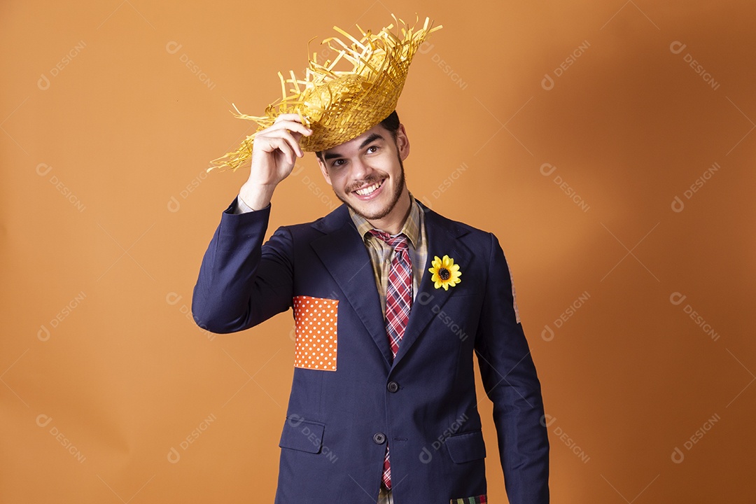Jovem rapaz sorridente vestido a caráter para festa junina com chapéu nas mãos