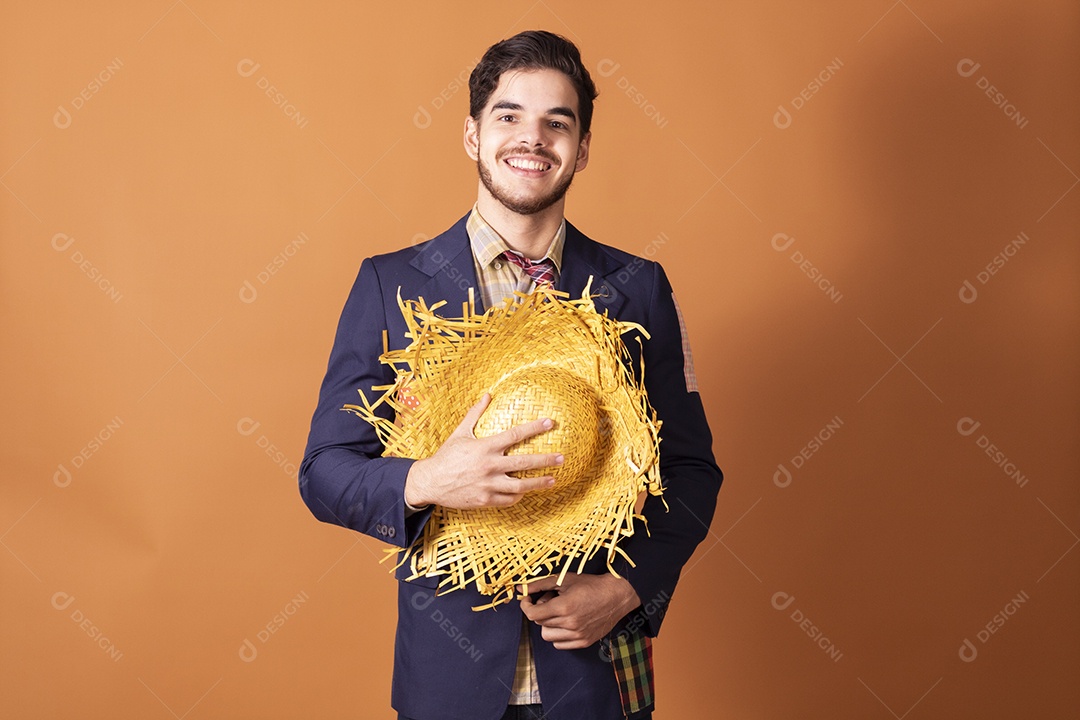 Jovem rapaz vestido a caráter para festa junina com chapéu nas mãos