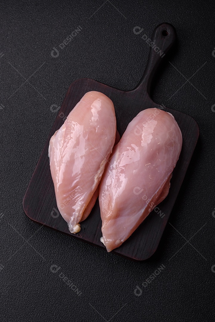 Filé de frango fresco sobre uma mesa de concreto escuro com especiarias e ervas. Preparação para cozinhar pratos de carne