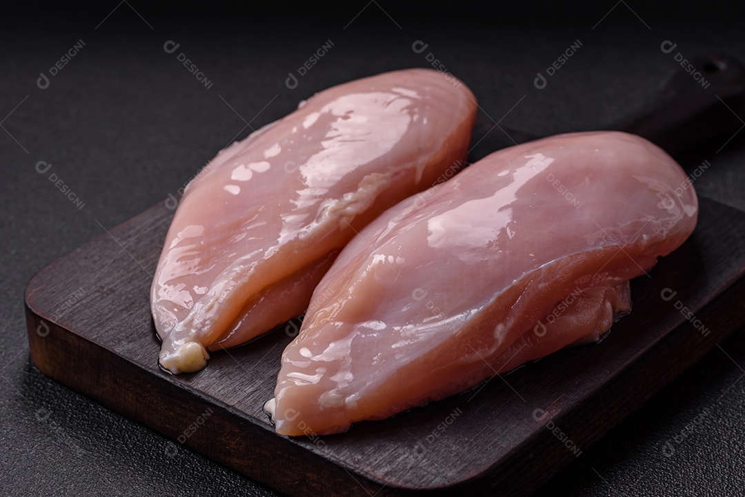 Filé de frango fresco sobre uma mesa de concreto escuro com especiarias e ervas. Preparação para cozinhar pratos de carne