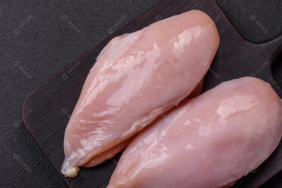 Filé de frango fresco sobre uma mesa de concreto escuro com especiarias e ervas. Preparação para cozinhar pratos de carne