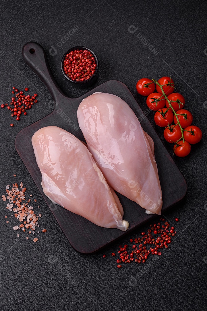 Filé de frango fresco sobre uma mesa de concreto escuro com especiarias e ervas. Preparação para cozinhar pratos de carne