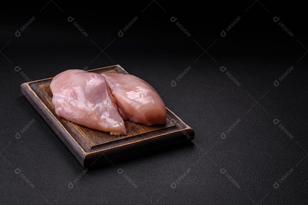 Filé de frango fresco sobre uma mesa de concreto escuro com especiarias e ervas. Preparação para cozinhar pratos de carne